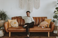 a man sitting on a brown couch with pillows